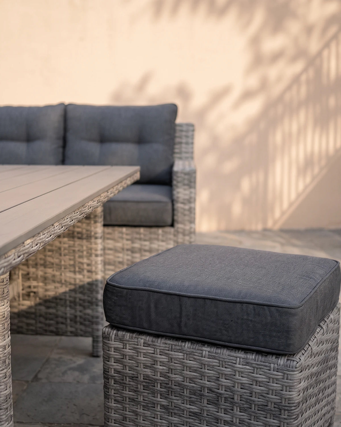 Close-up of the Atrico Lounge Set wicker stool with grey cushion beside the coffee table